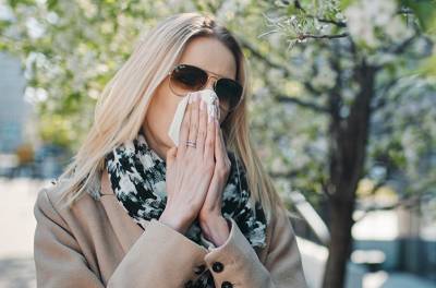 Allerginen nuha vai flunssa? Nuori nainen kärsii allegisesta nuhasta ja niistää vuotavaa nenäänsä.