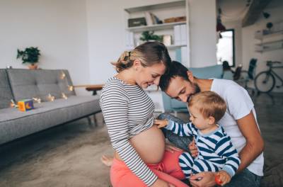 Miten raskaus vaikuttaa krooniseen migreeniin? Pieni poika istuu isänsä sylissä ja koskettaa raskaana olevan äitinsä vatsaa.