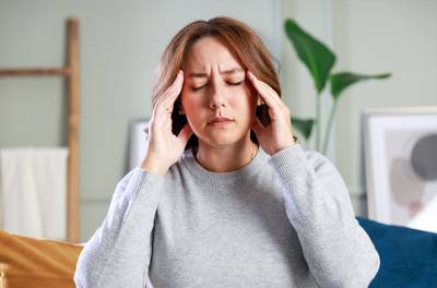 Mitä tapahtuu ennen migreenikohtausta ja sen jälkeen. Nainen painaa sormilla ohimoitaan.