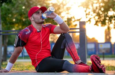 Vinkit kesähelteille. Nesteytys urheilun ja muun hikoilun yhteydessä. Lippalakkipäinen mies pitää juomataukoa. Kuva Getty Images
